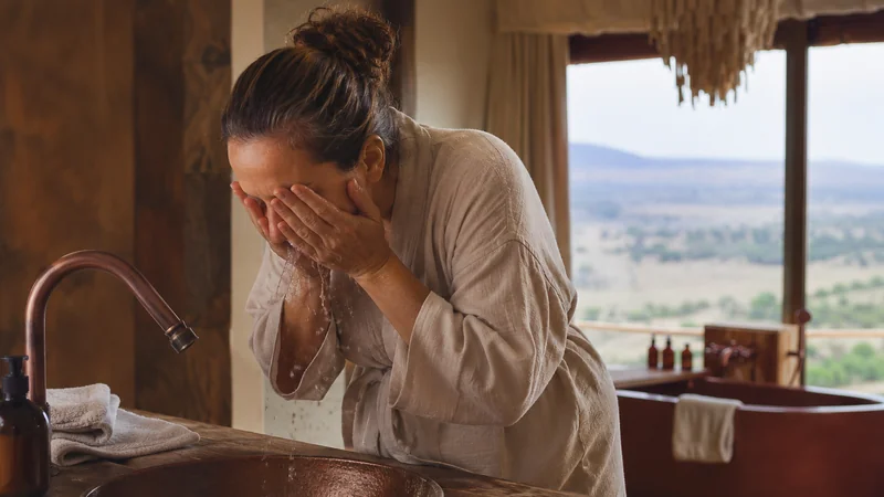 Femme se passant de l’eau fraîche sur le visage devant un lavabo
