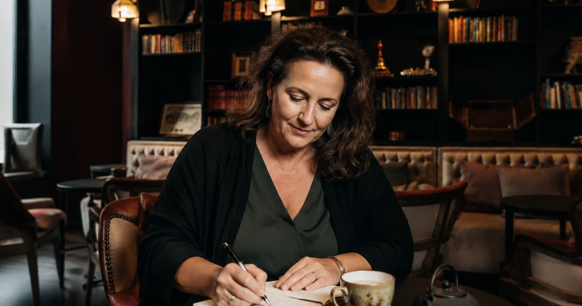 Femme écrivant dans un carnet dans un intérieur chaleureux, illustrant le retour au calme et l'observation de soi