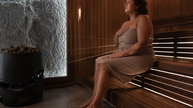 Femme assise dans un sauna, les yeux fermés et une main posée sur la poitrine