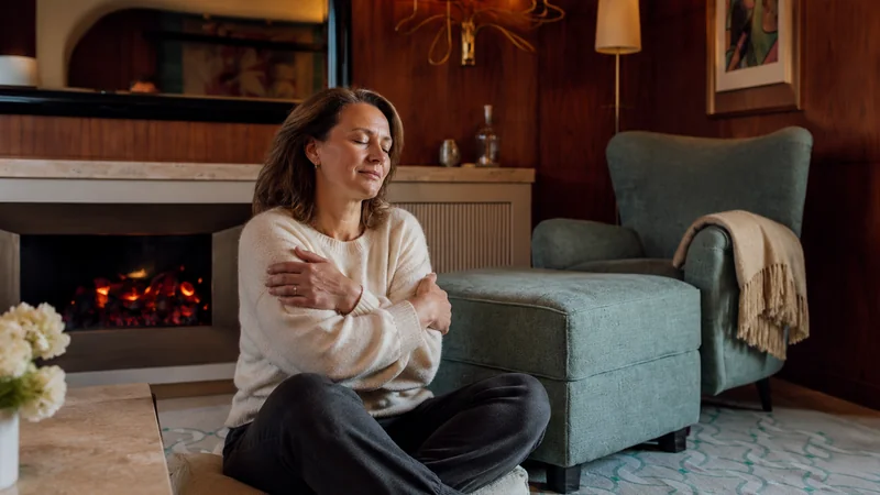 Femme assise près d’une cheminée, les bras croisés autour d’elle