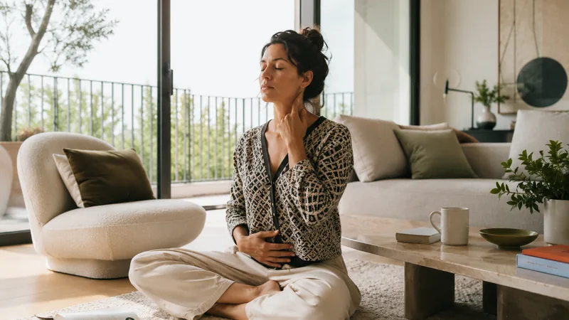 Femme assise au sol, les yeux fermés, une main au cou et l’autre au ventre
