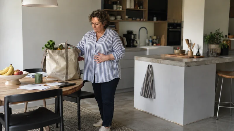 Femme dans sa cuisine, main sur le ventre, illustrant les troubles digestifs liés à un tonus vagal faible
