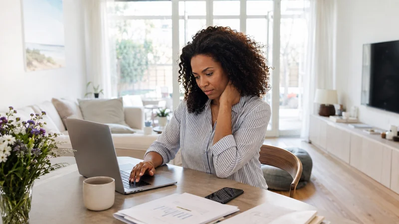 Femme au laptop, main sur la nuque, illustrant l'état d'alerte et le stress chronique