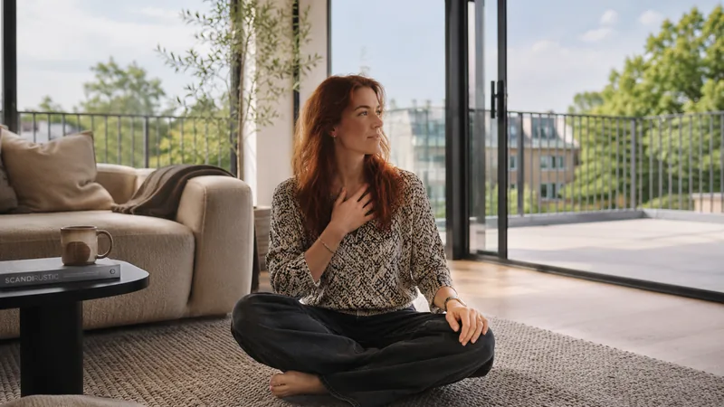 Femme assise au sol, une main sur la poitrine, dans un intérieur lumineux