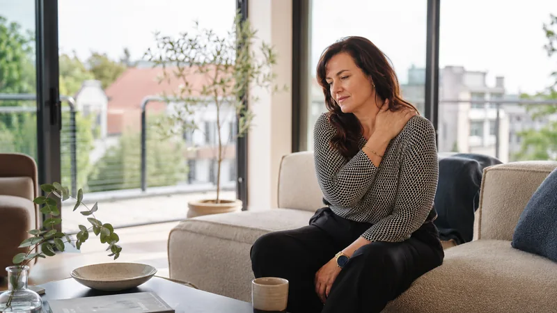 Femme touchant son cou assise dans un salon lumineux